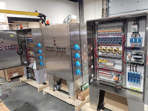 Three stainless steel control panels partially assembled in a production shop