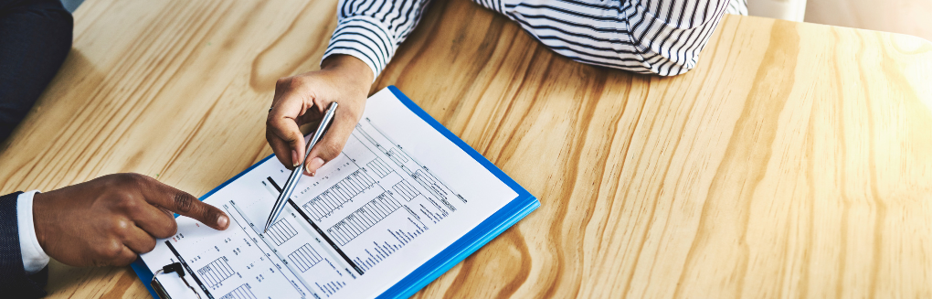 two people review a printed report on a table while one of them points with a pen