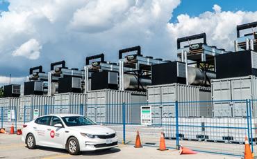 Several containerized 1MW standby generators in a row with a T&T company sedan parked in front